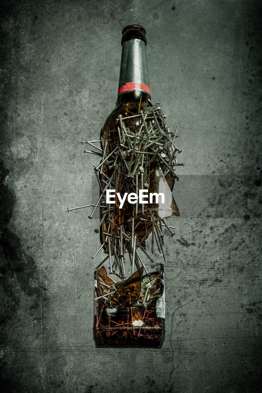 Close-up of damaged bottle with nails against wall