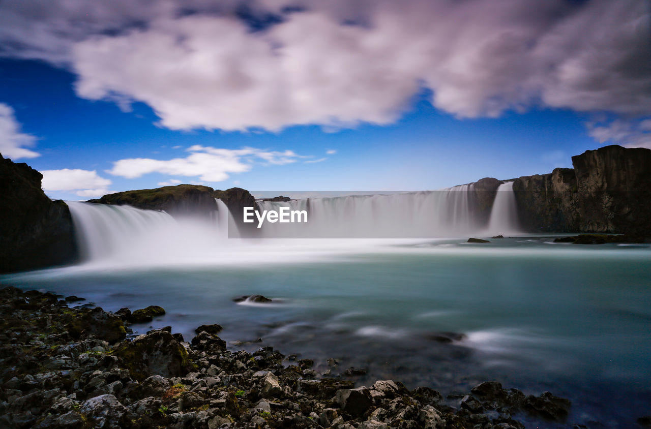 Scenic view of waterfall against cloudy sky