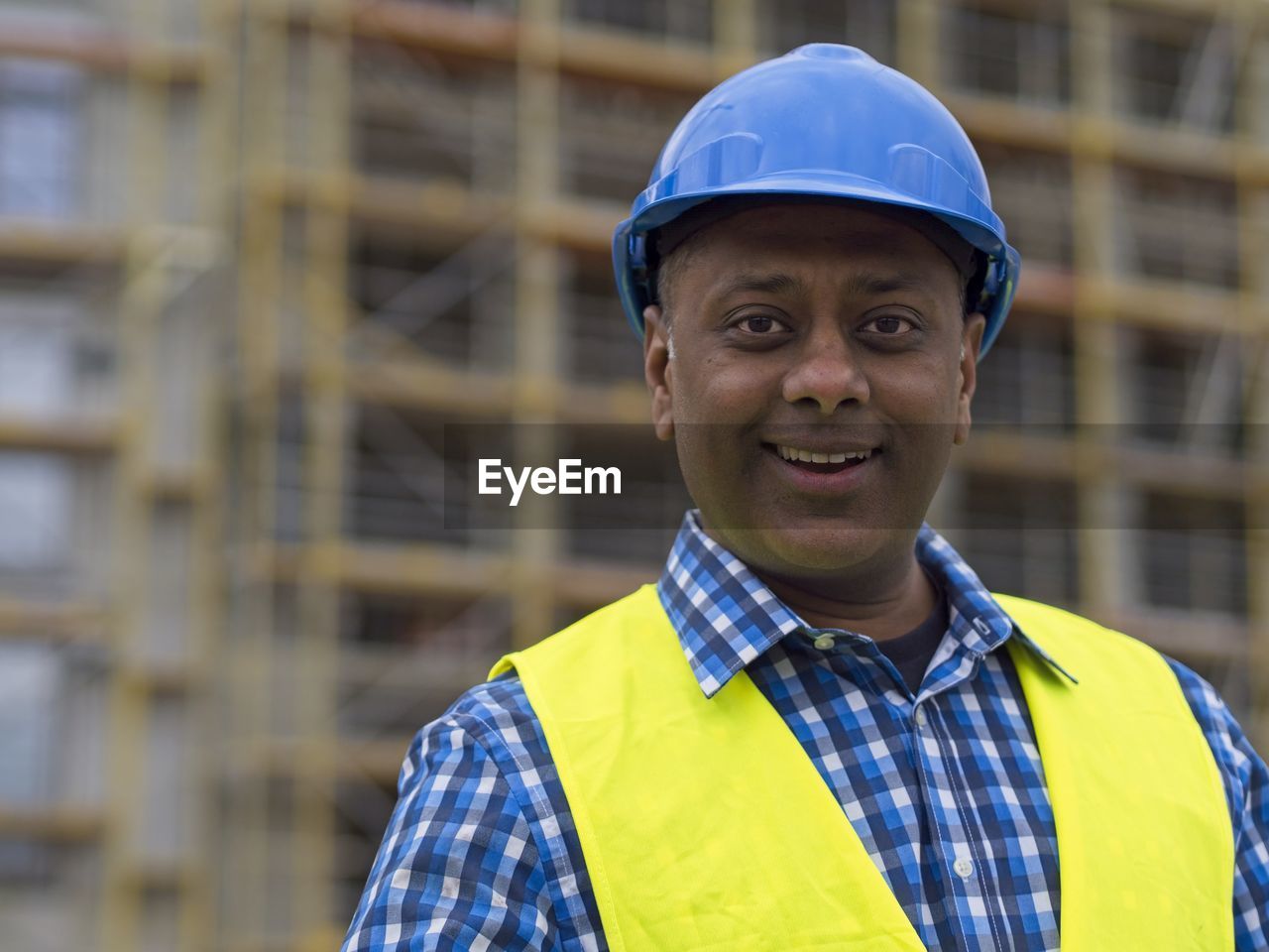 Smiling indian civil engineer or factory worker wearing a blue helmet and looking at camera