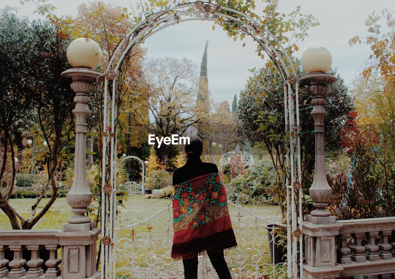 Rear view of woman standing against metal gate in park against sky