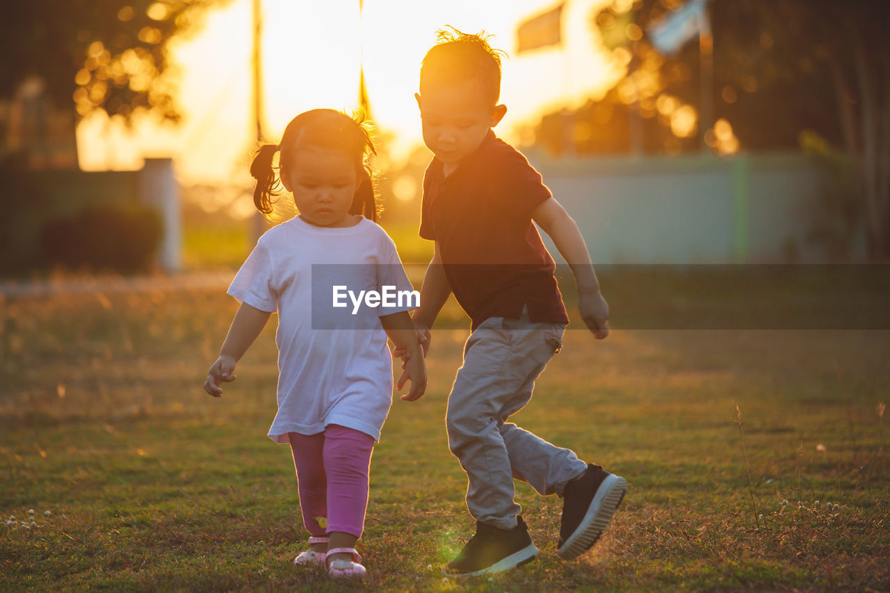 Full length of brother and sister holding hands in park