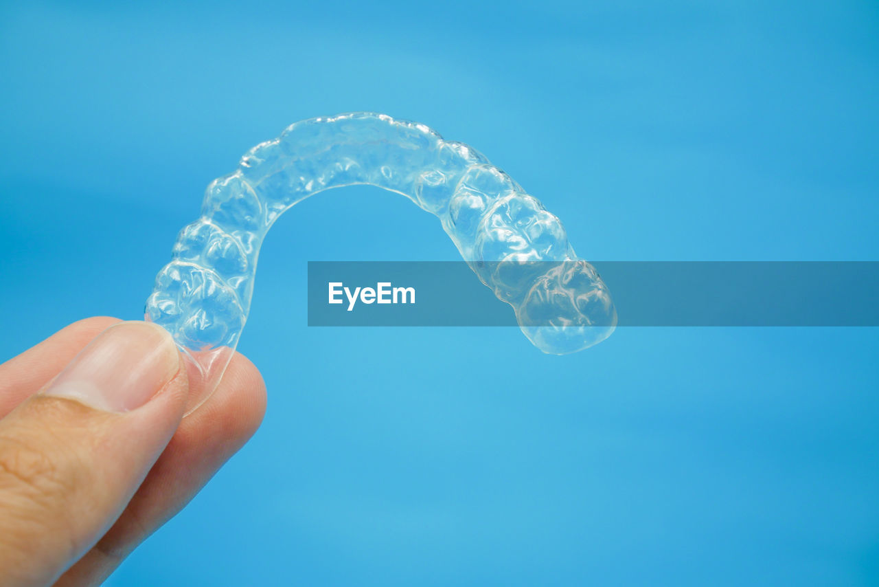 Cropped hand holding dental aligner against blue background