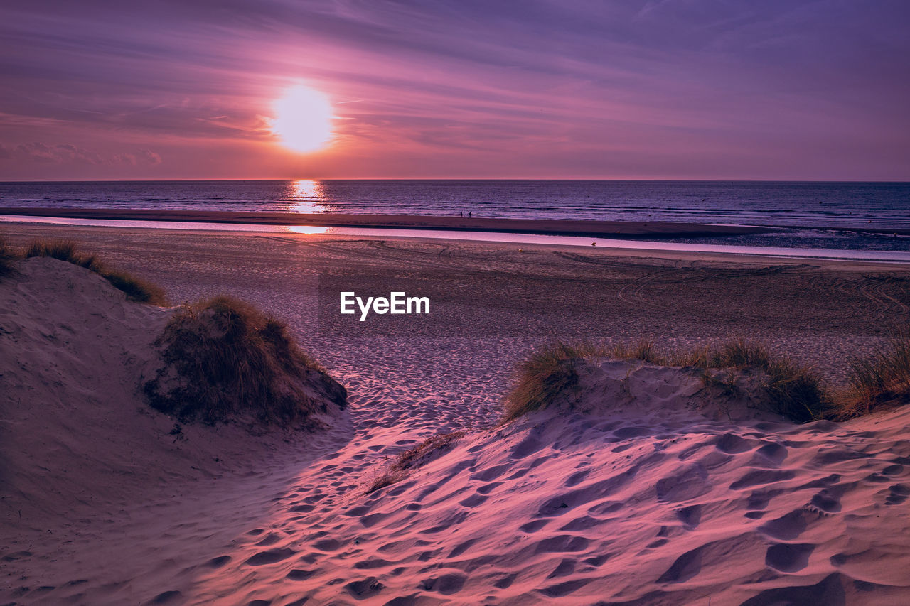 Small path leading from marram grass covered dunes towards the beach prior to a colorful sunset