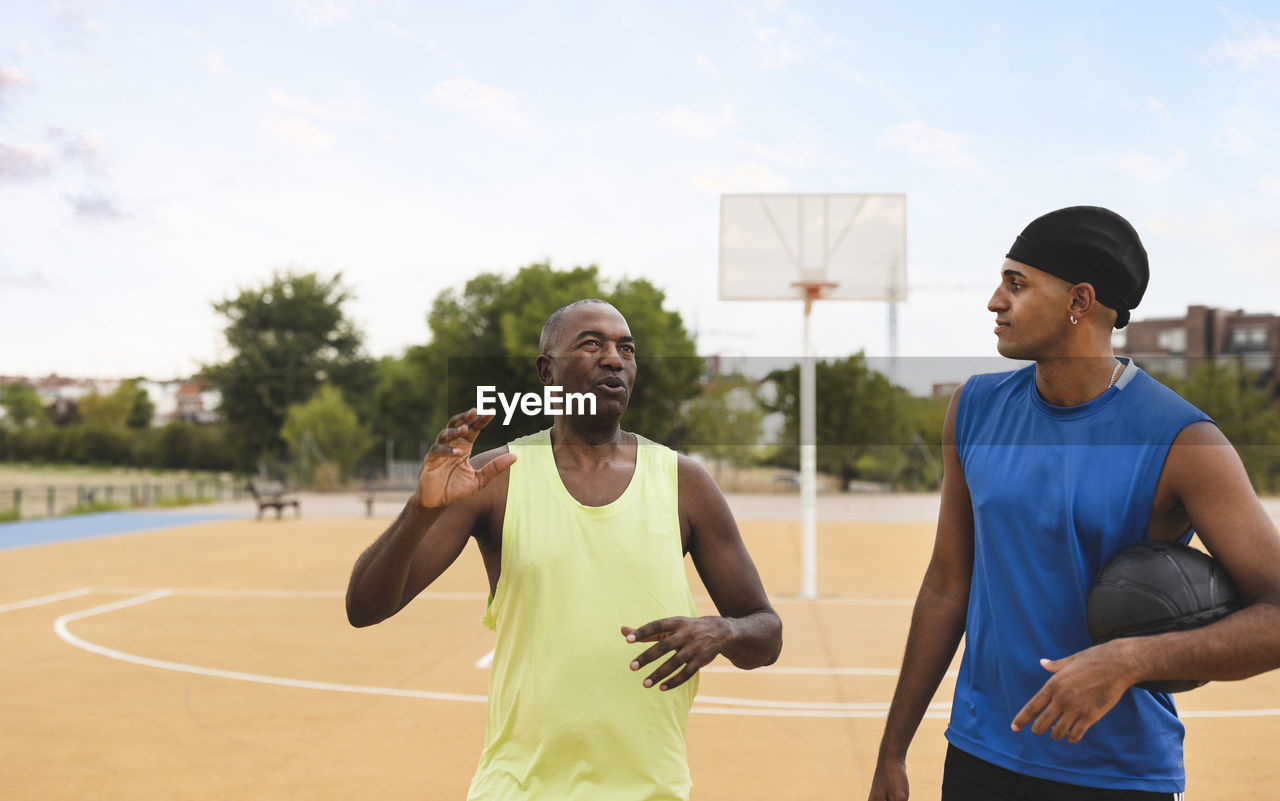 Mature man talking with son at basketball court