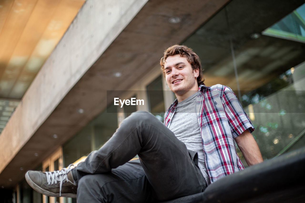 Low angle view portrait of young man sitting on a bench