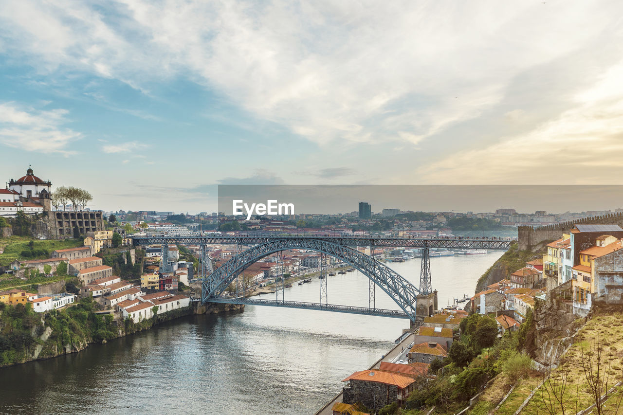 Bridge over river amidst buildings in city against sky