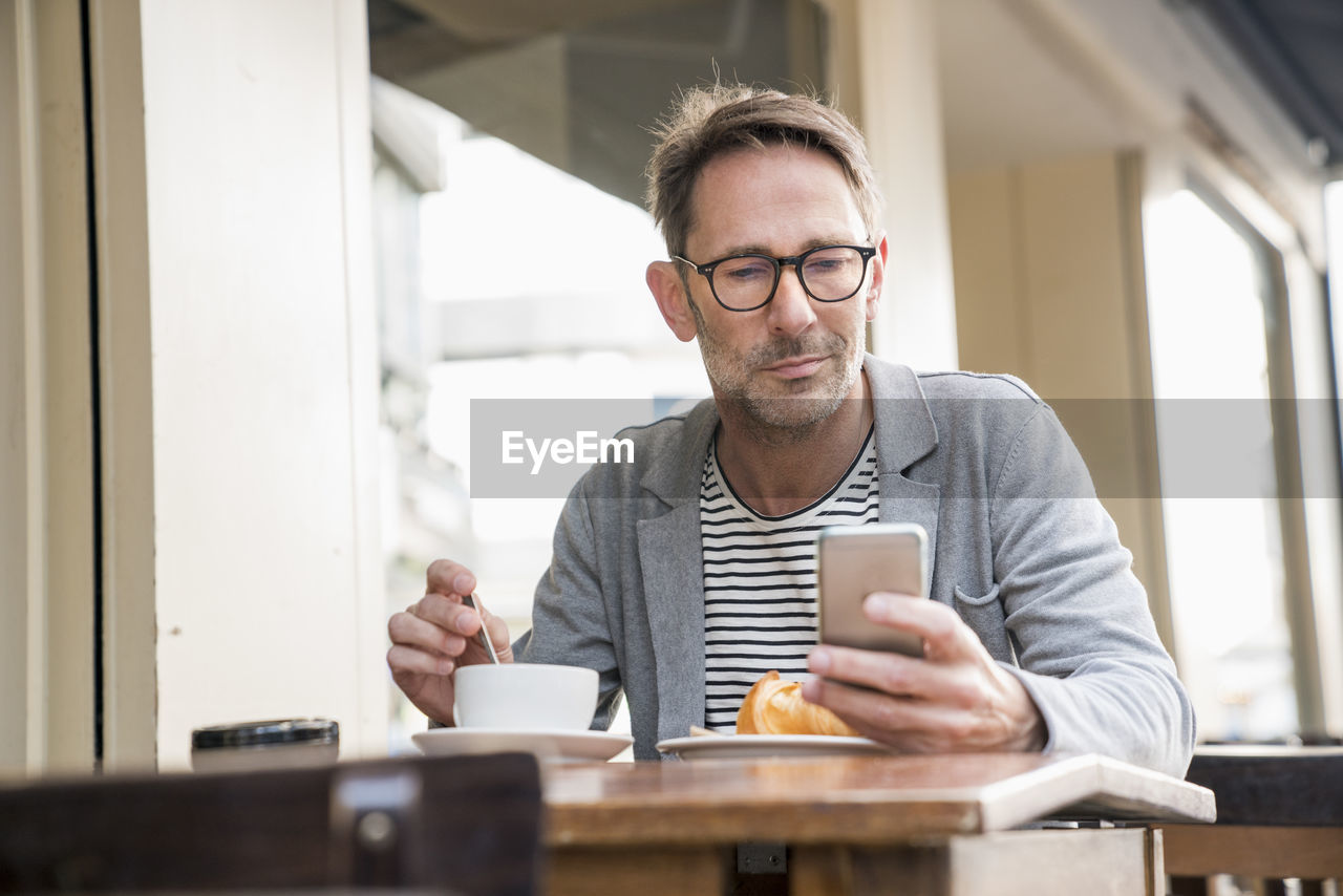 Portrait of mature man sitting at sidewalk cafe looking at cell phone