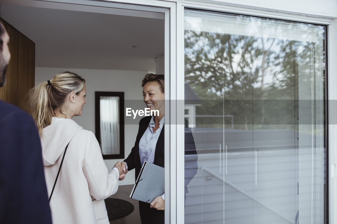 Smiling female real estate agent greeting couple in new house