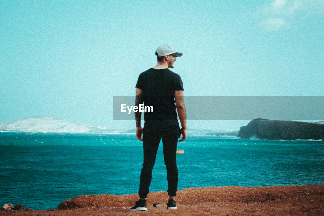 Rear view of man standing at beach against sky