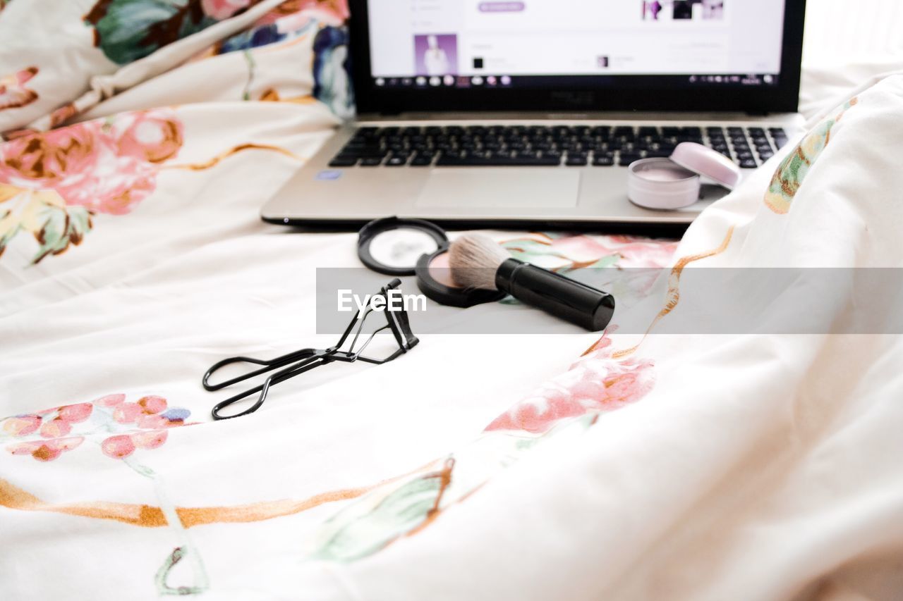 High angle view of laptop with beauty products on bed