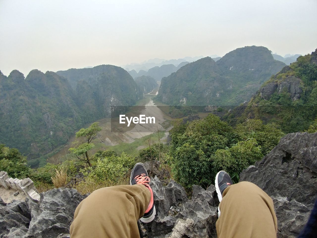 Low section of man sitting on cliff against valley