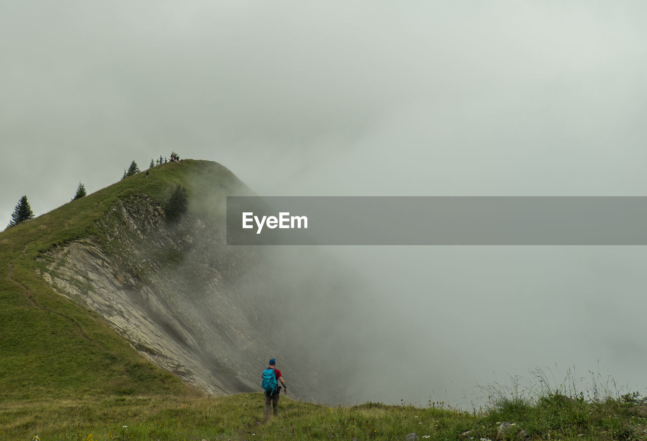 High angle view of man with backpack hiking on mountain during foggy weather