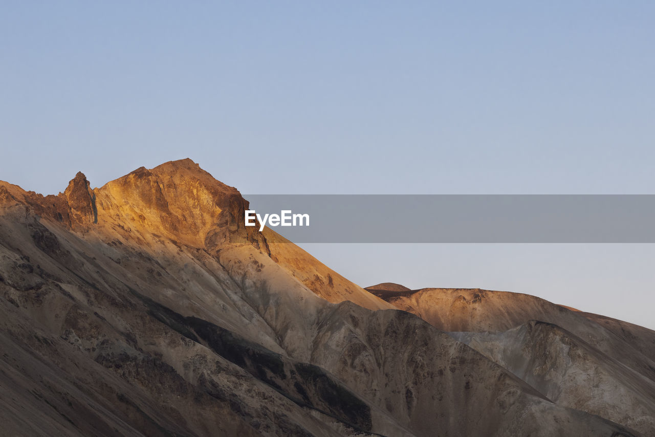 Spectacular landscape of endless rough rocky terrain with dry slopes and random vegetation located under clear blue sky in iceland