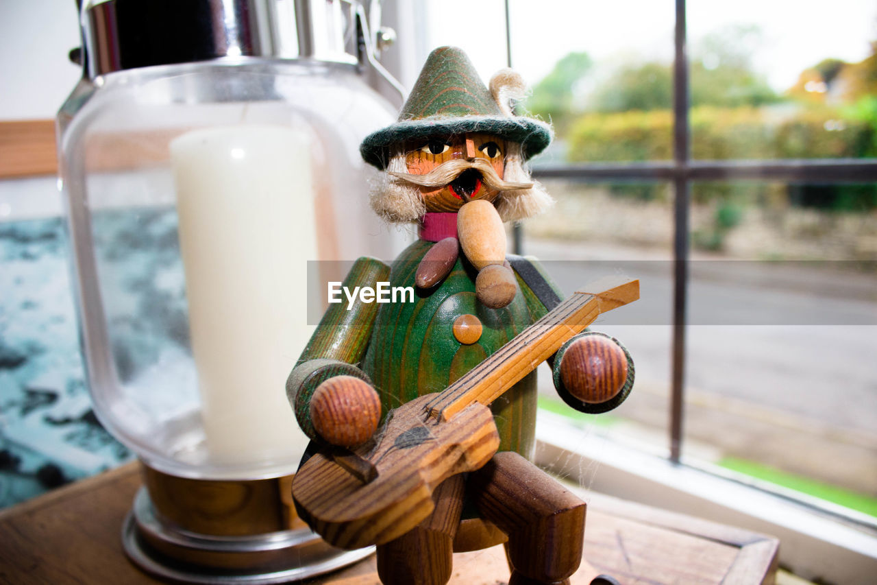 Close-up of wooden figurine by lantern against window
