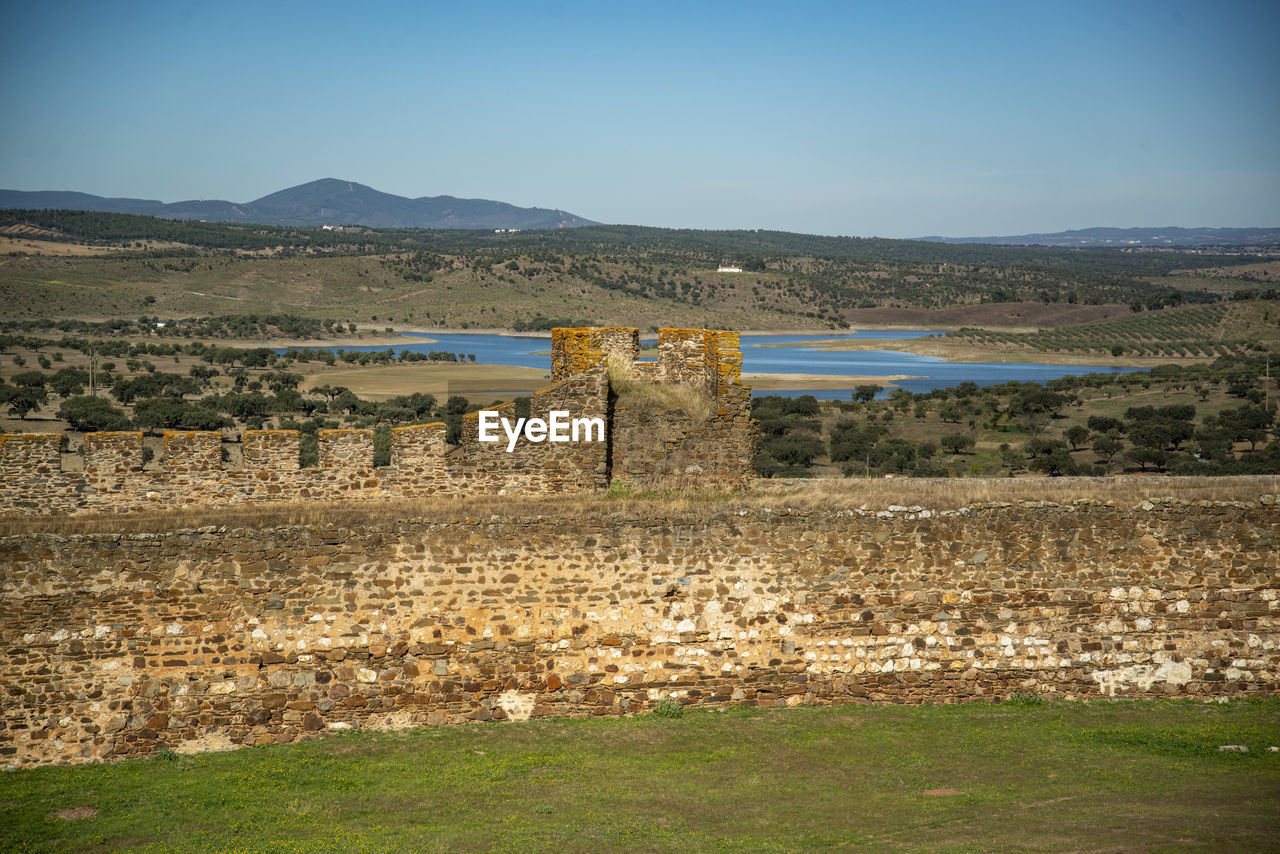 rural area, architecture, hill, landscape, nature, ruins, sky, environment, history, sea, no people, built structure, land, water, scenics - nature, the past, travel destinations, plant, travel, ancient, ancient history, wall, reflection, grass, day, outdoors, clear sky, beauty in nature, tranquility, rock, blue, tranquil scene, tourism, stone wall, building exterior, coast, building, cloud