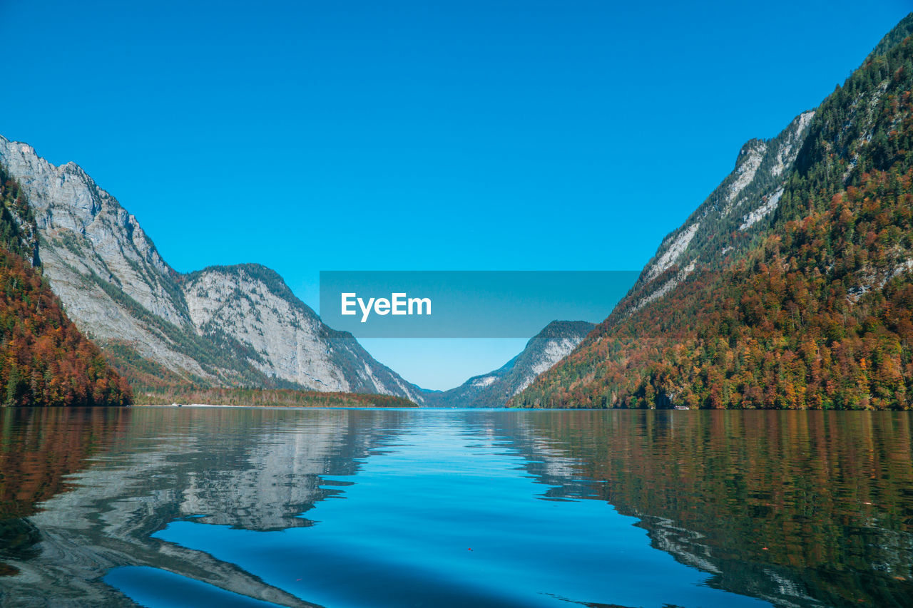 Scenic view of lake by mountains against clear blue sky