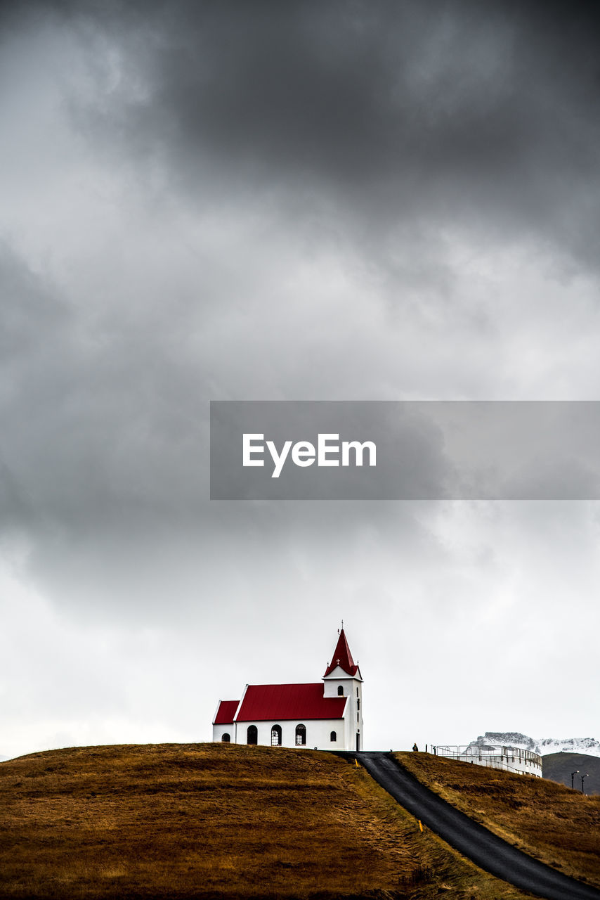 Wooden church on field by building against dramatic sky