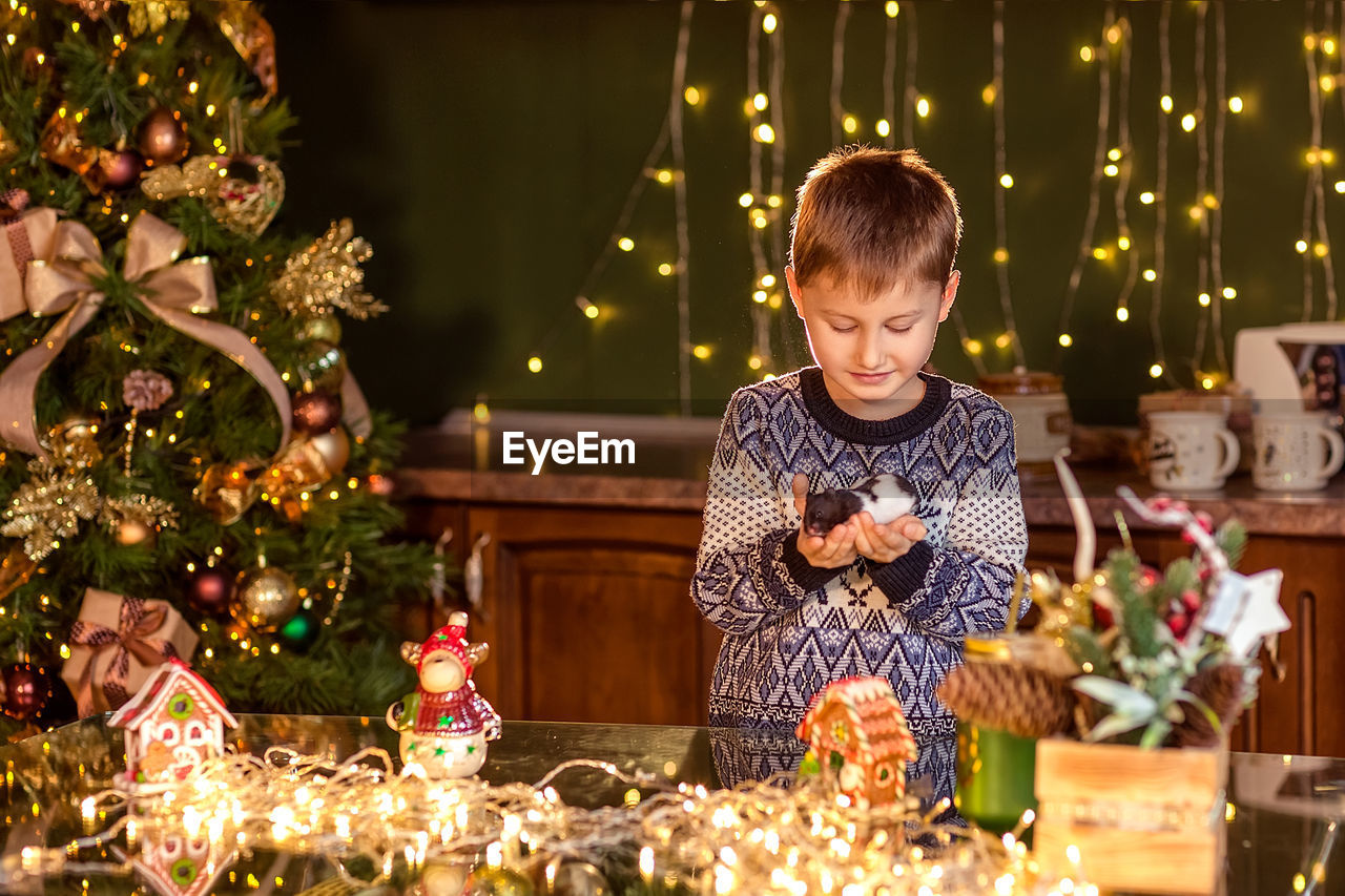 FULL LENGTH OF BOY HOLDING CHRISTMAS TREE AT ILLUMINATED SHOP