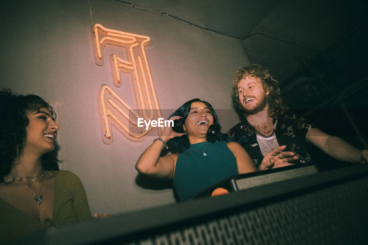 Happy young female dj dancing amidst friends while enjoying weekend at nightclub