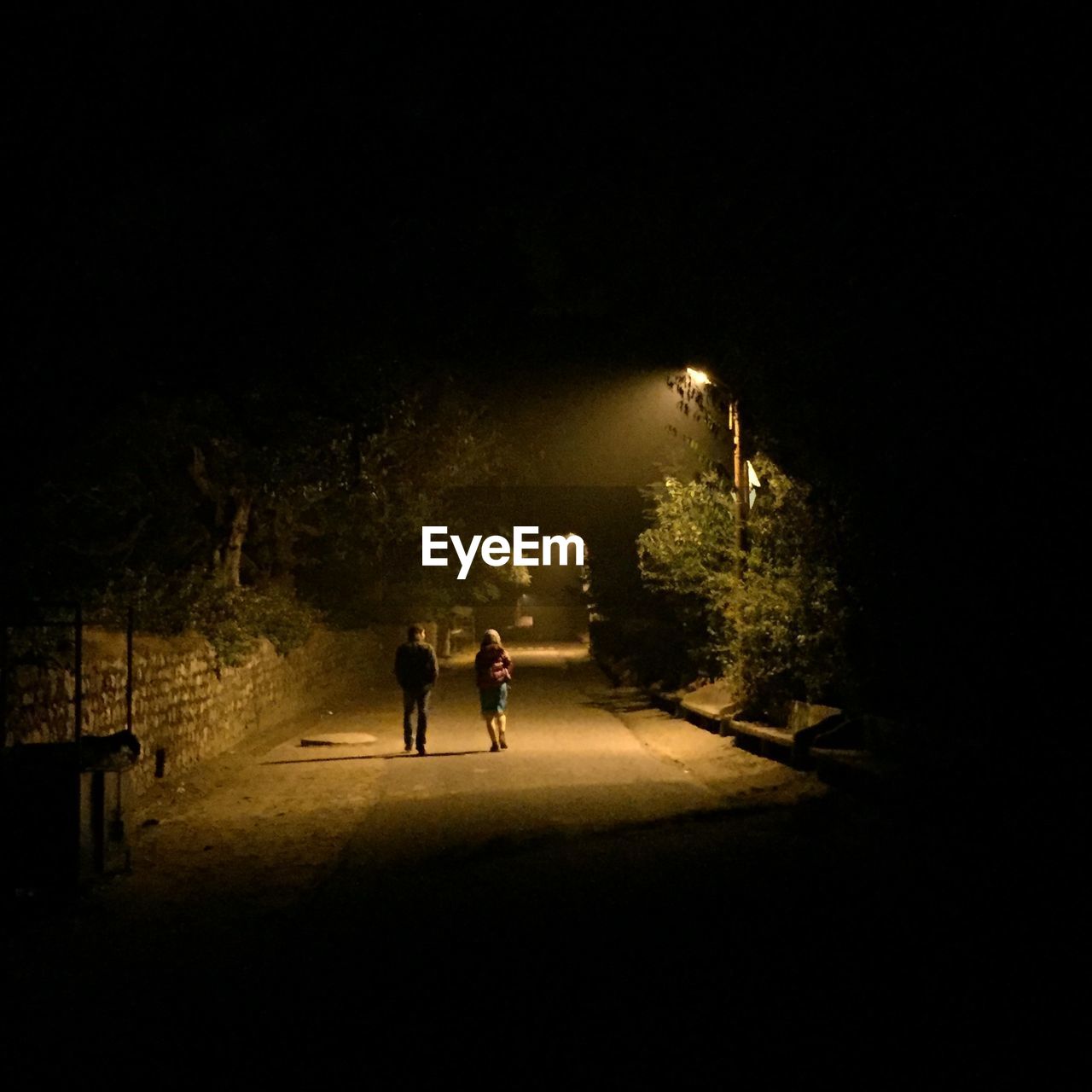 FULL LENGTH REAR VIEW OF WOMAN WALKING IN ILLUMINATED PARK