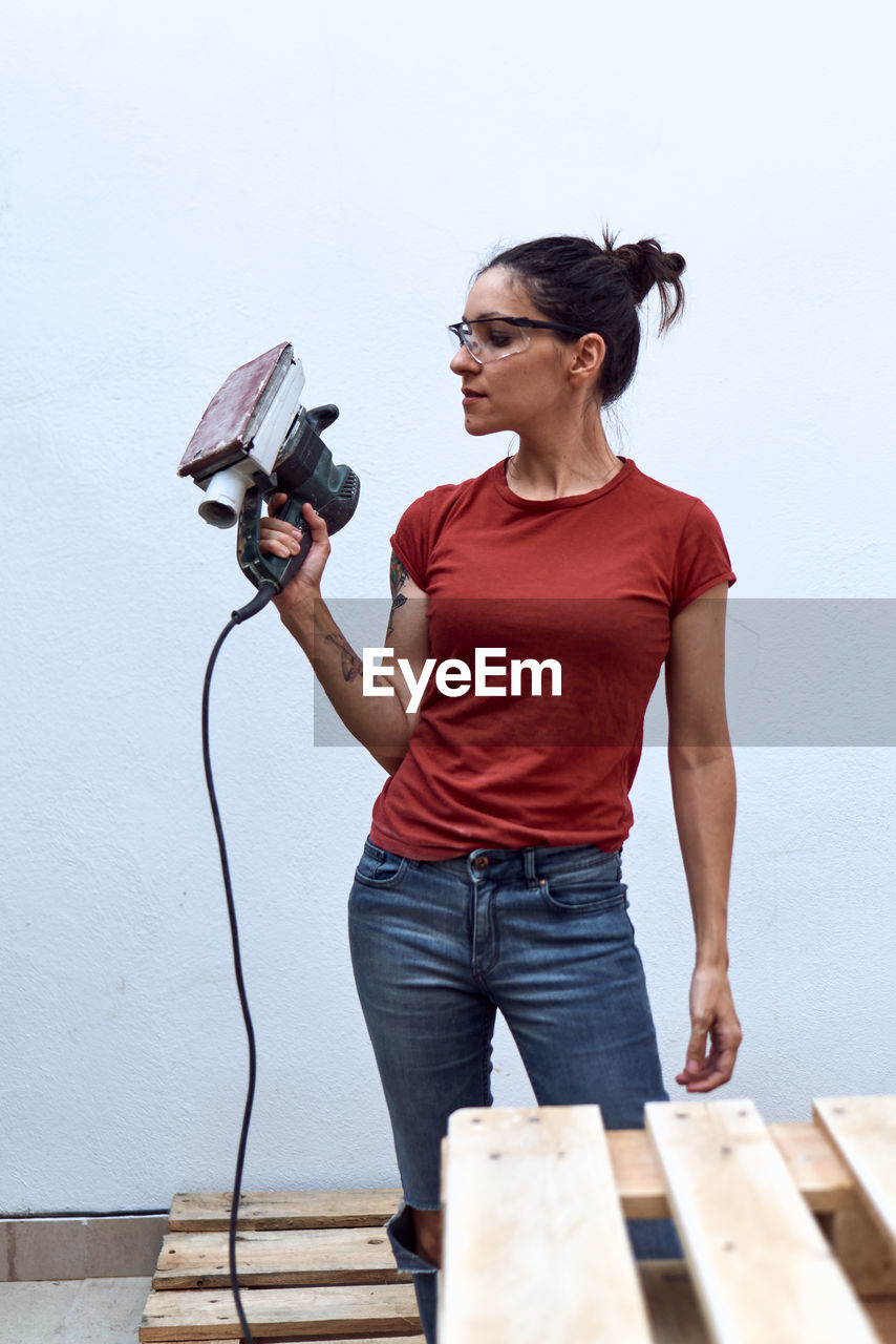 Young woman with a power sander on a white background.