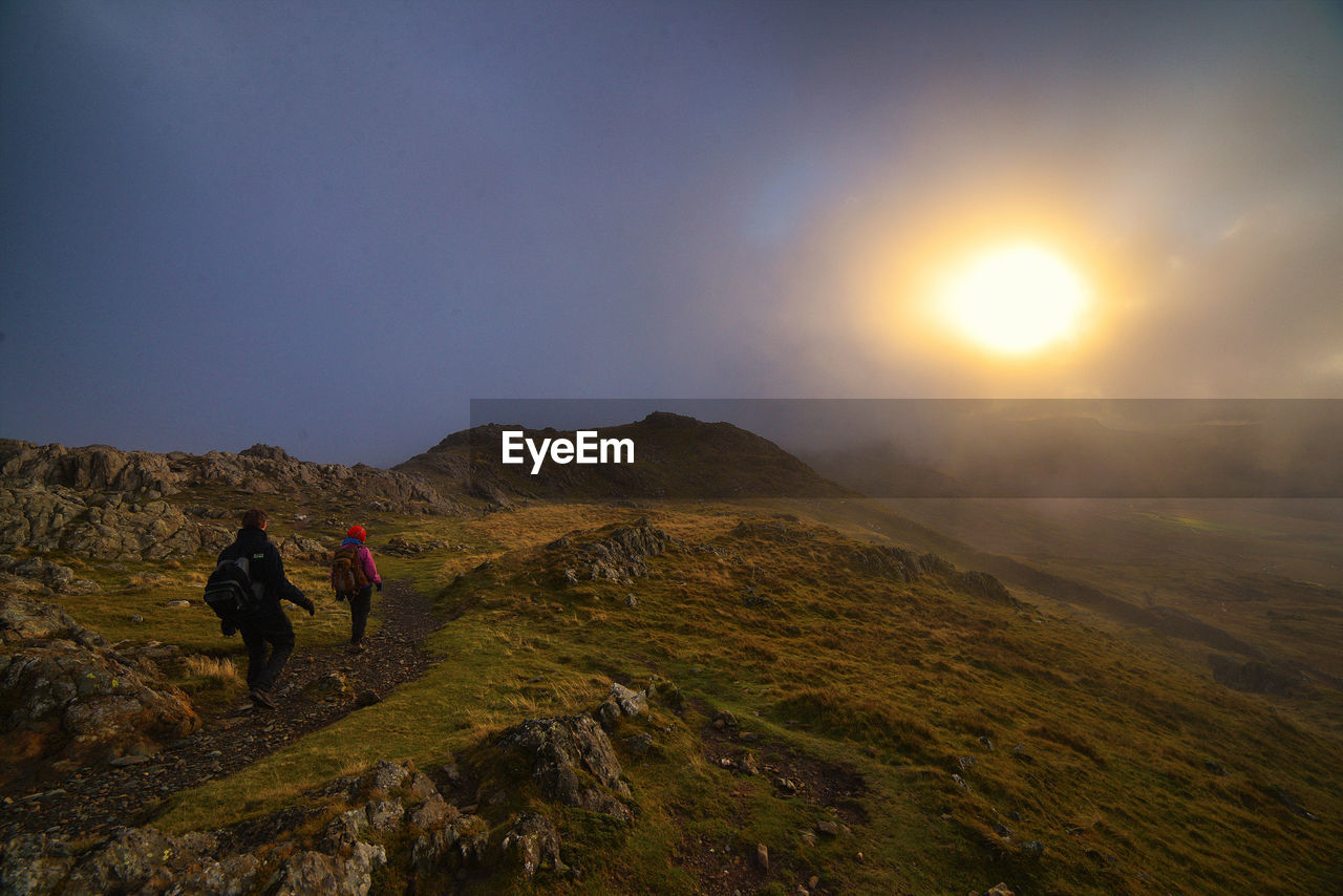 Rear view of hikers walking on mountains during sunset