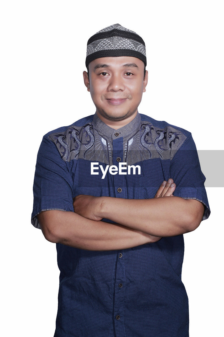 Portrait of man in traditional clothing standing with arms crossed against white background