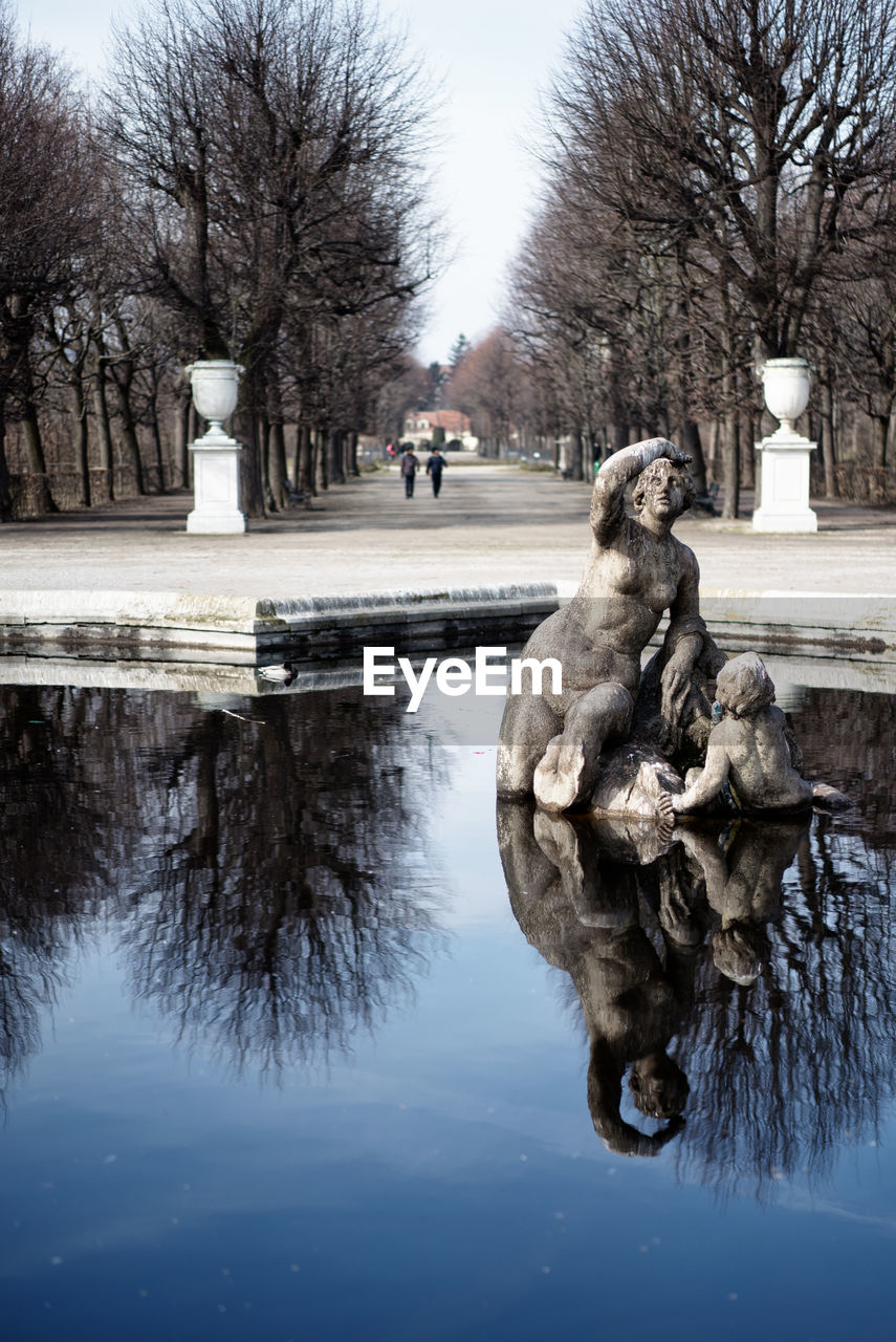 STATUE ON BARE TREE BY WATER