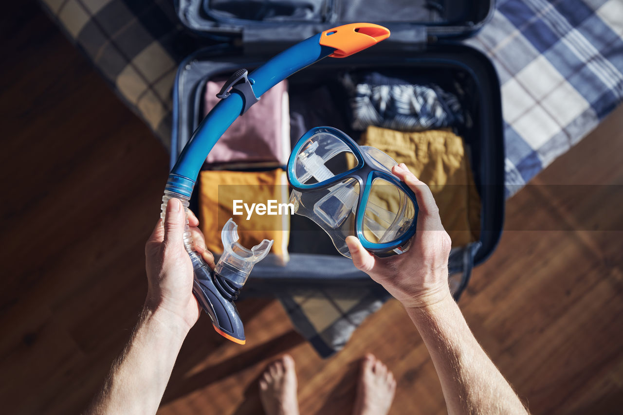 Young man holding snorkel and goggles in hands at home. packing suitcase and planning travel.