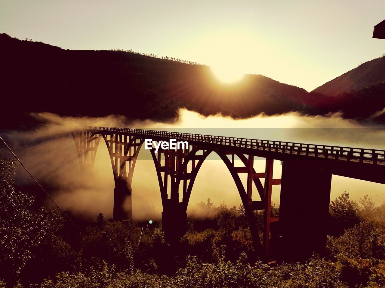 Silhouette bridge over mountains against sky during sunset