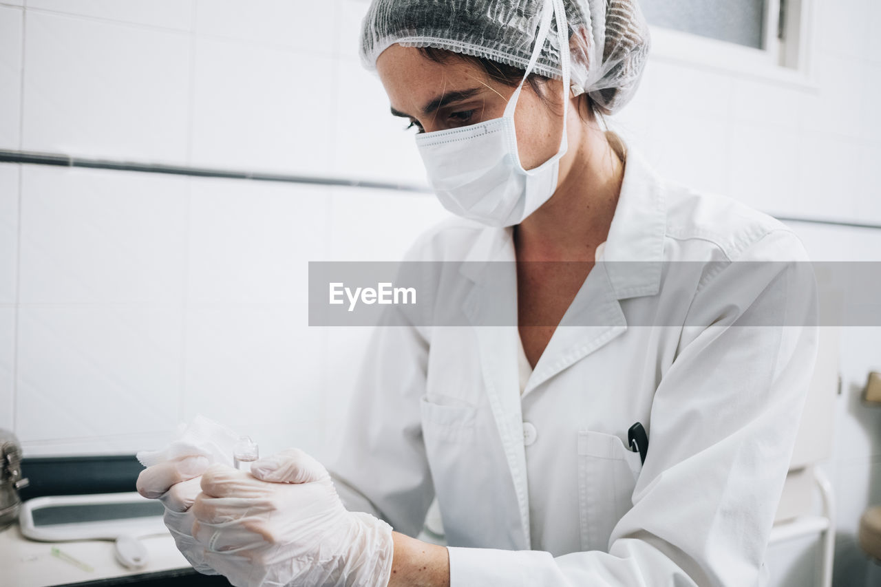 Doctor with a mask on her face and a plastic cap preparing gauze in a hospital operating room