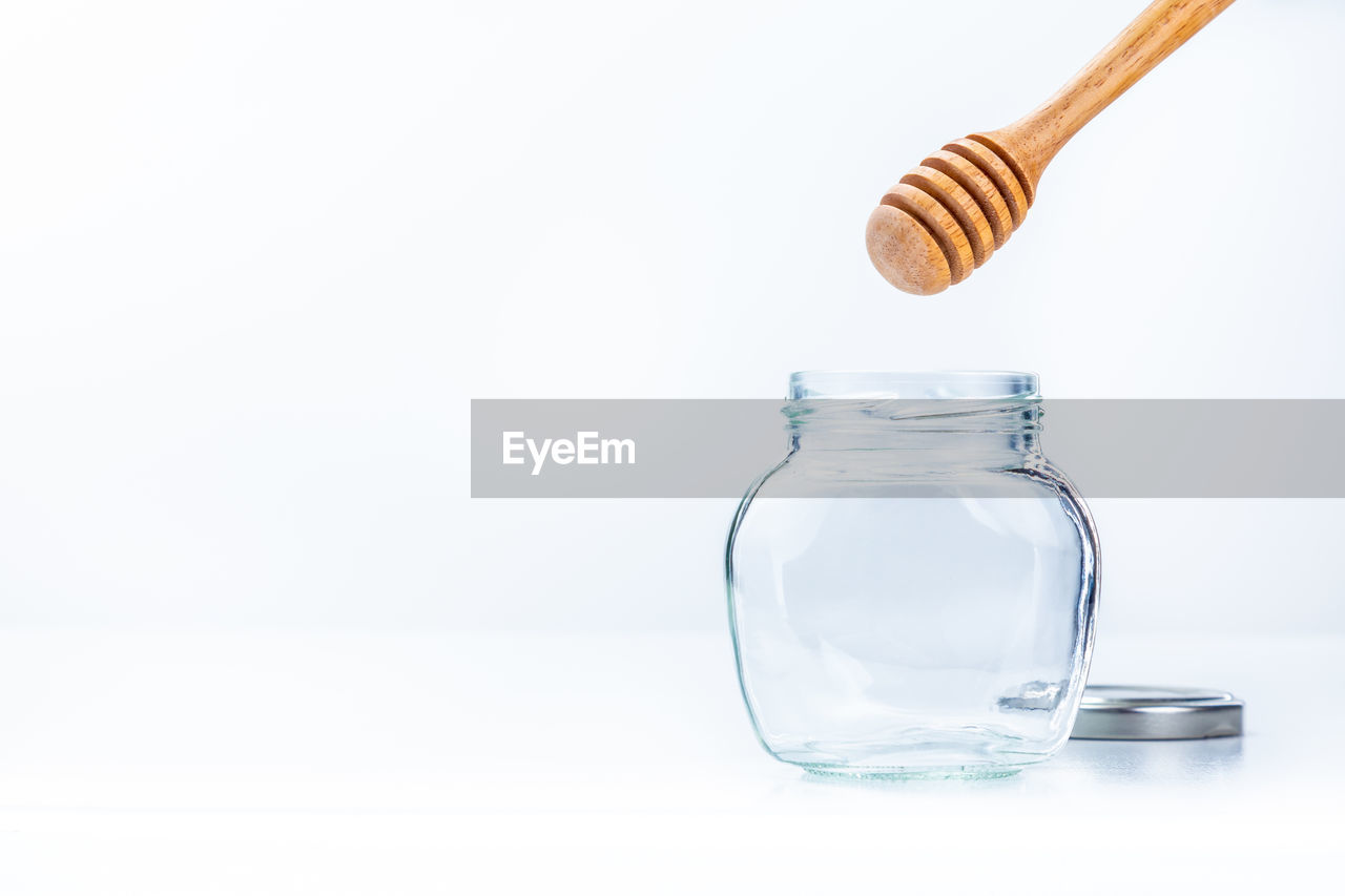 Wooden honey dipper over the empty glass jar on white background