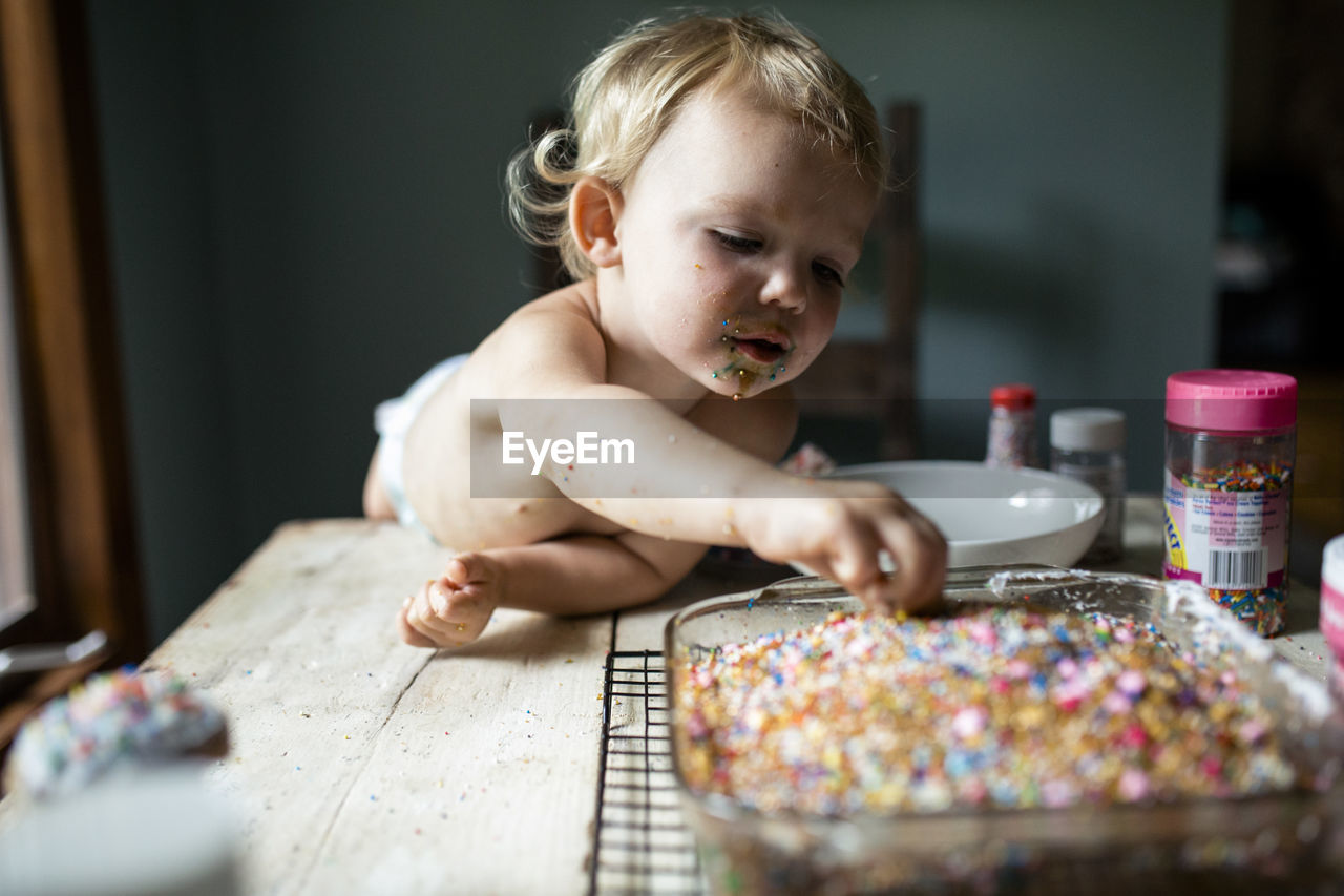 Toddler girl sneaking colorful sprinkles off of freshly baked cake