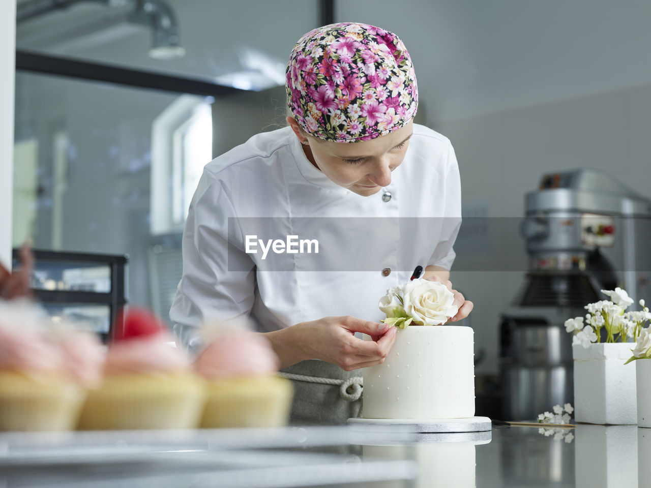 Young confectioner decorating cake with marzipan roses in kitchen