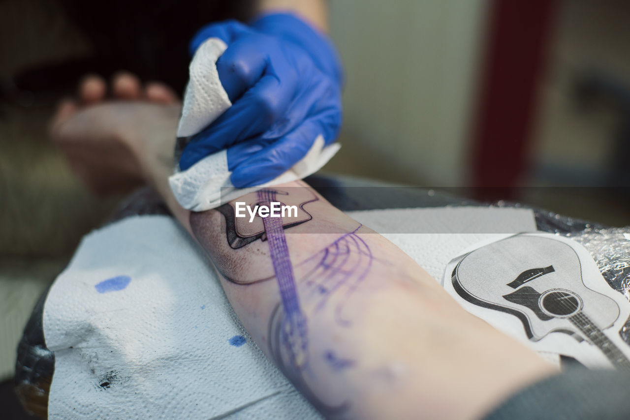 Cropped hand of artist tattooing on hand