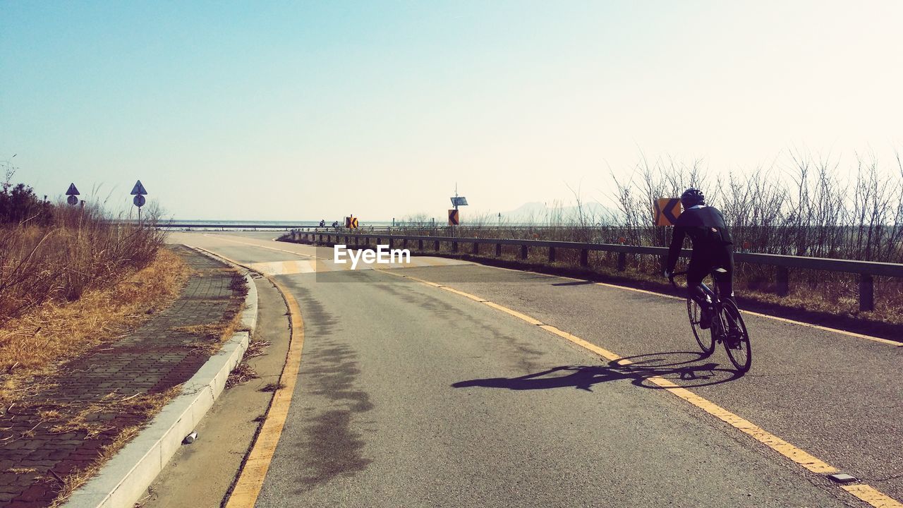 Rear view of man riding bicycle on road