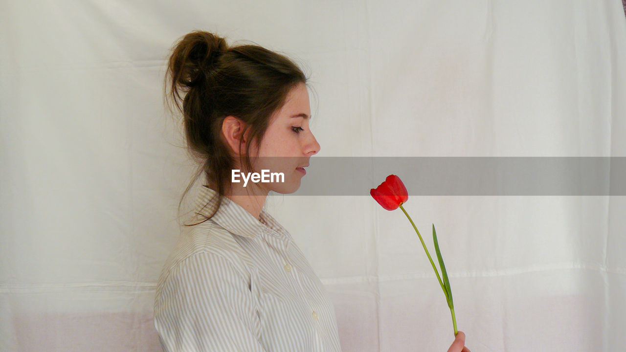 Woman holding red tulip against white wall