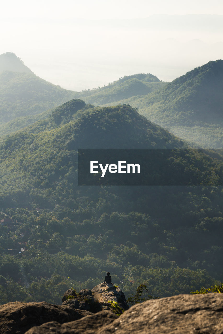 High angle view of man sitting on rock against mountains and sky