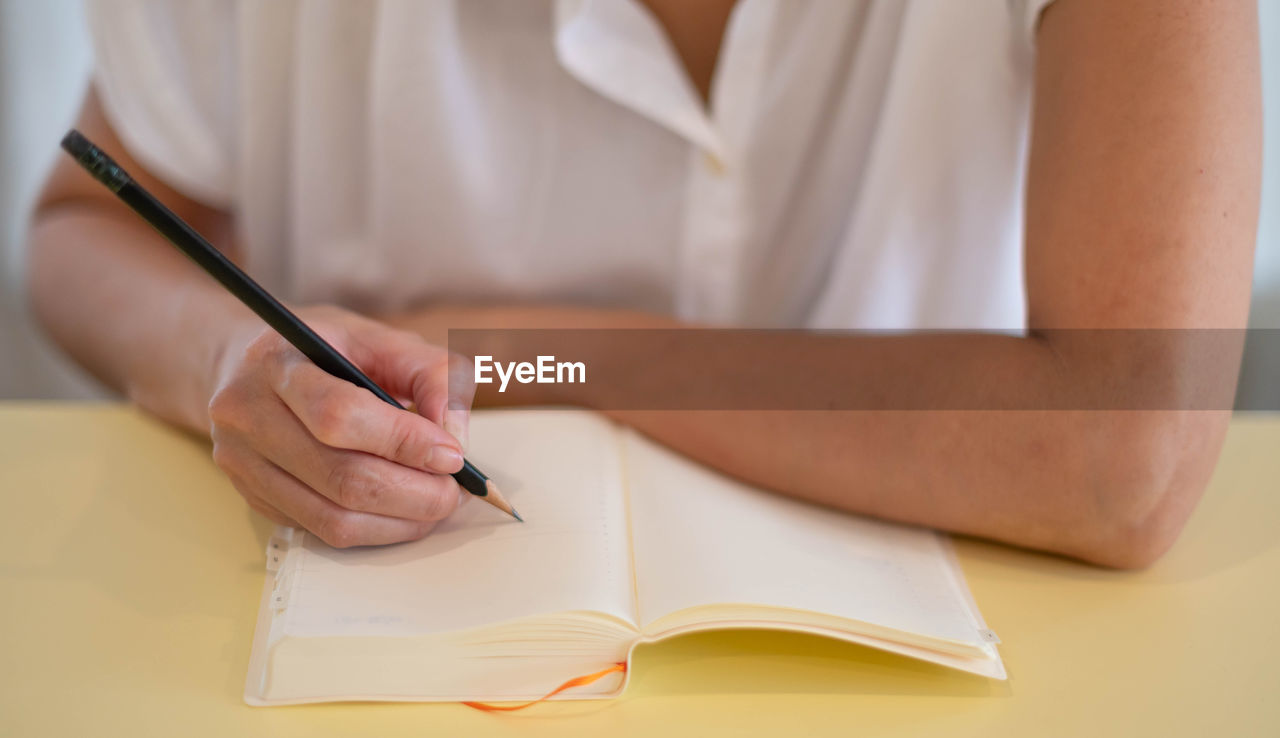 midsection of woman writing on book at table