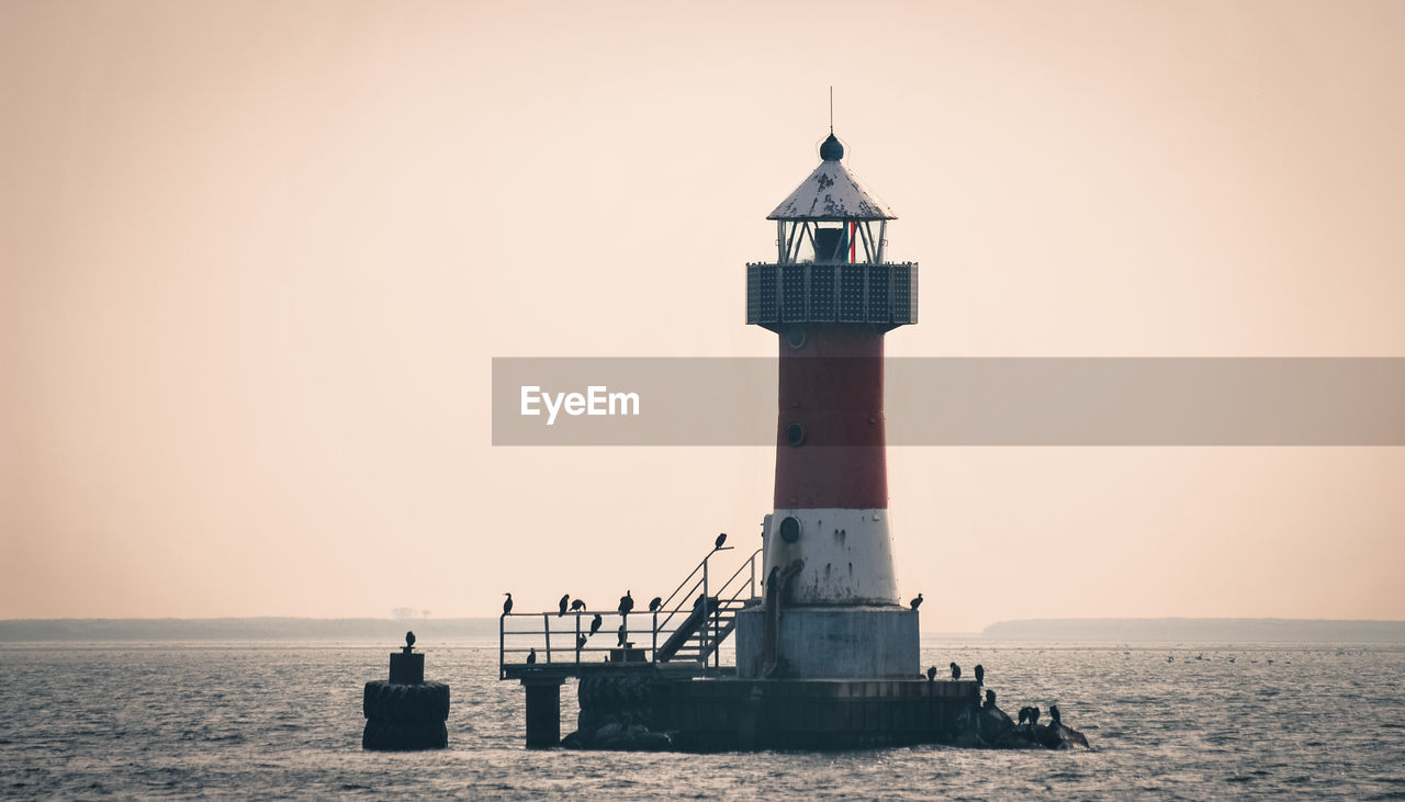 Lighthouse by sea against clear sky