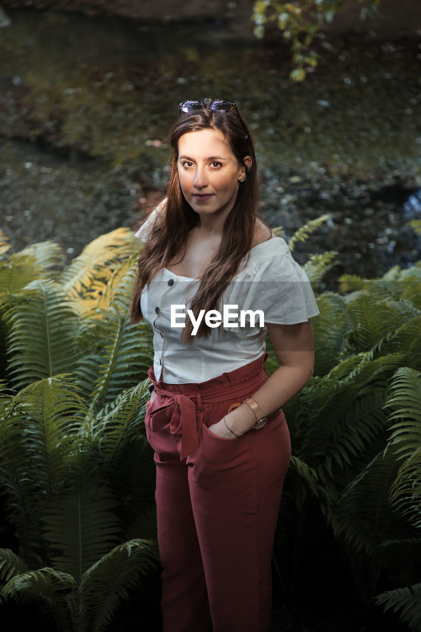 PORTRAIT OF WOMAN STANDING AGAINST PLANTS