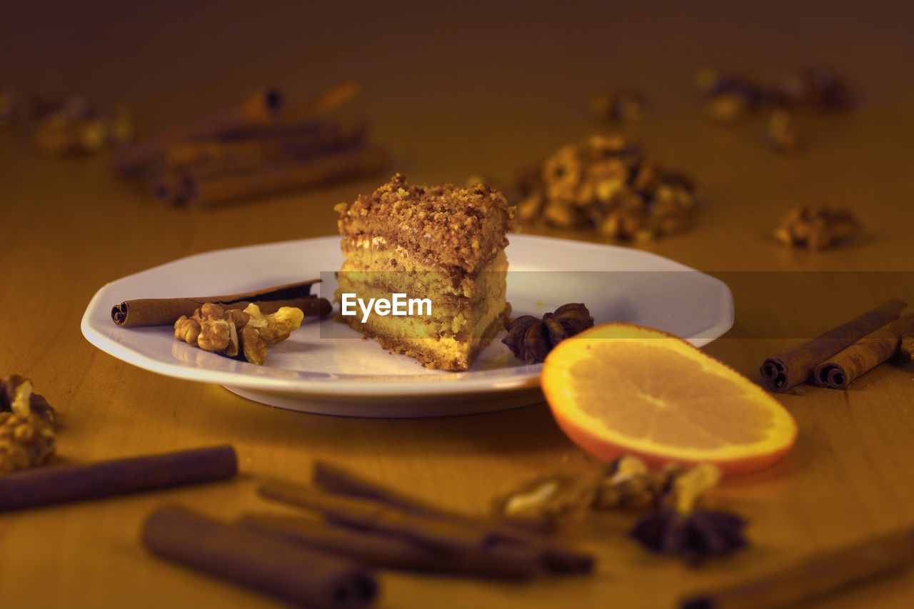 Close-up of honey cake served in plate on table with orange, nuts, cinnamon and anise