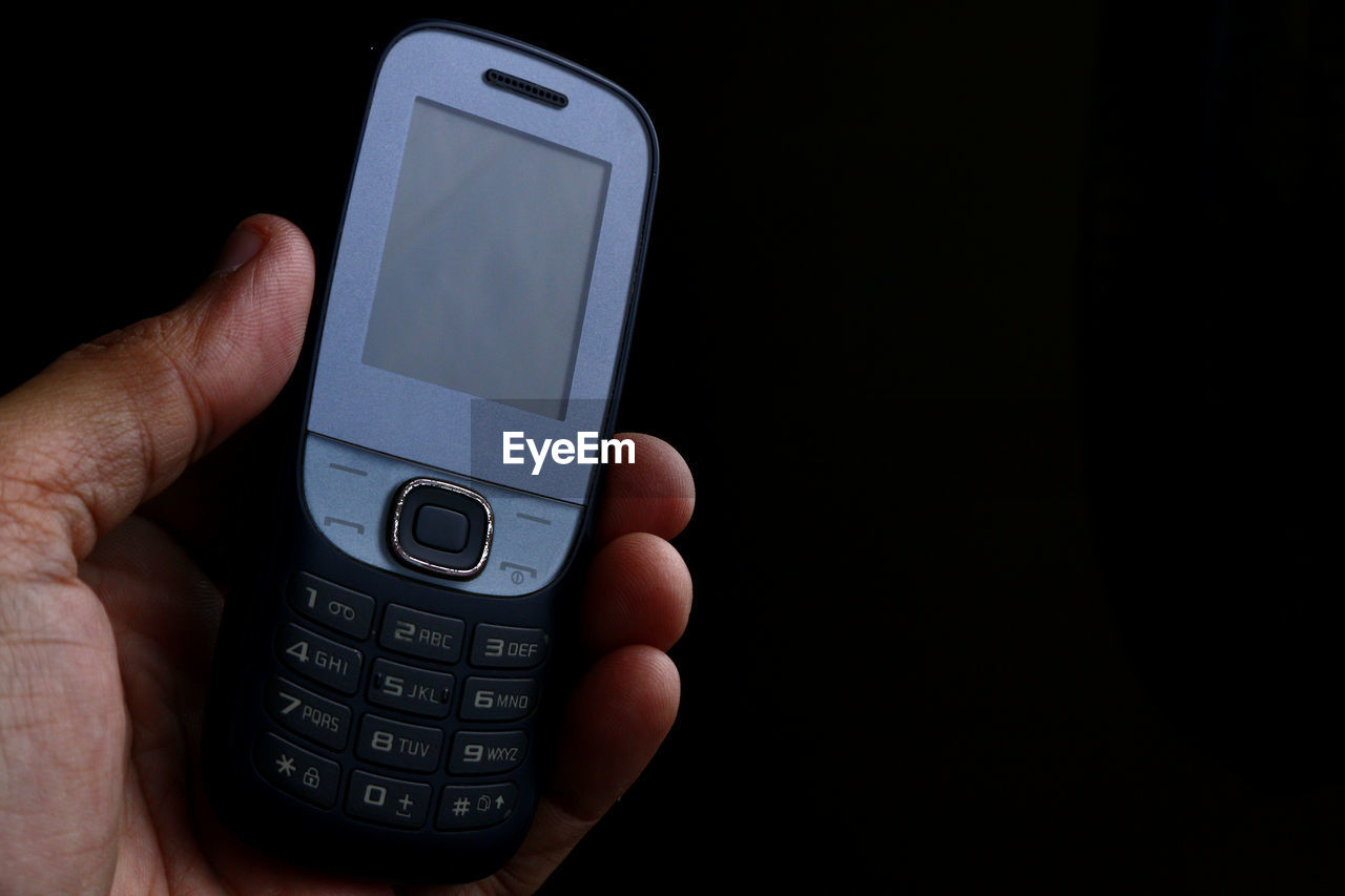 Cropped hand of person holding smart phone against black background