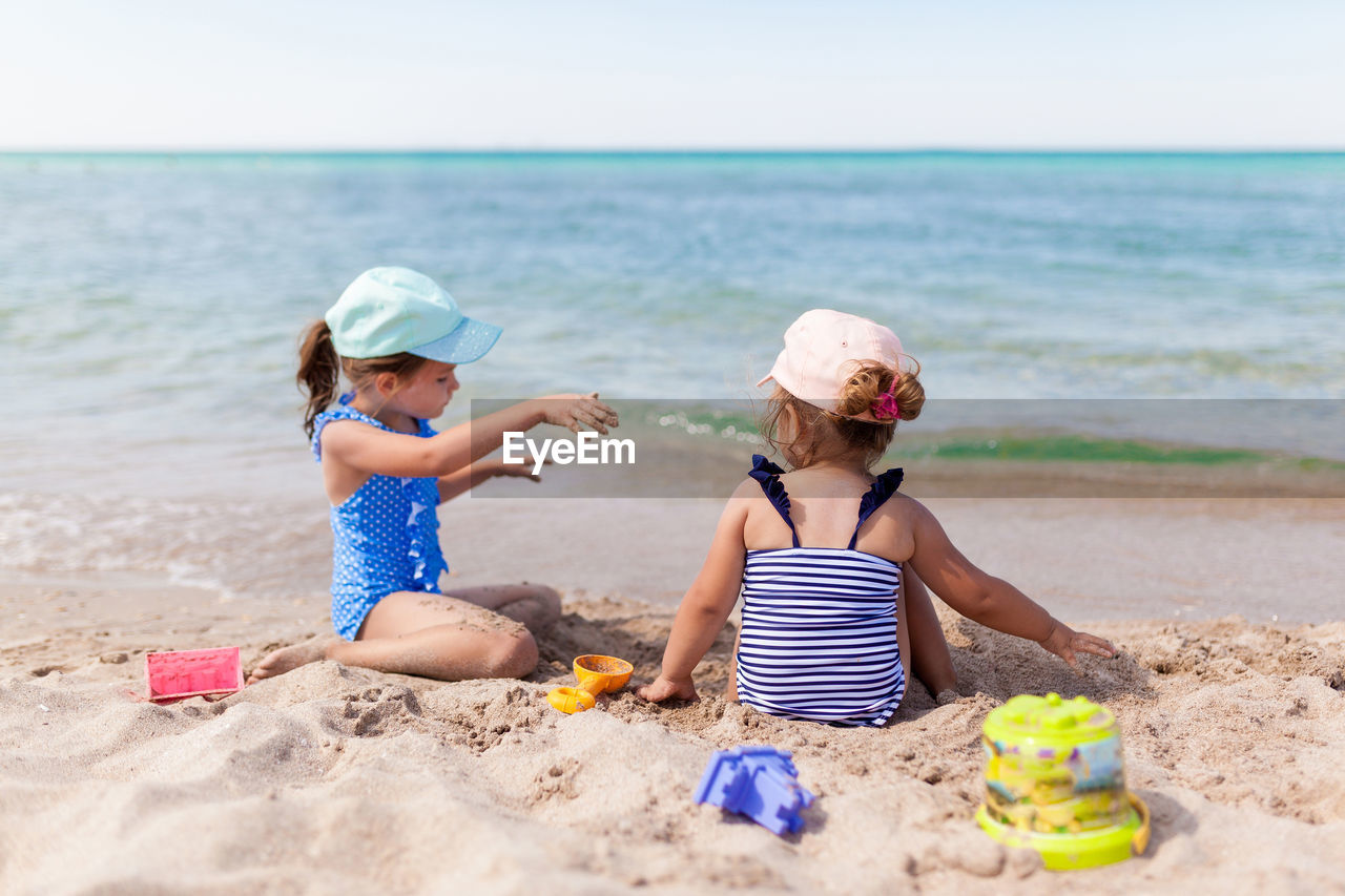 Girls playing with sand while sitting at beach