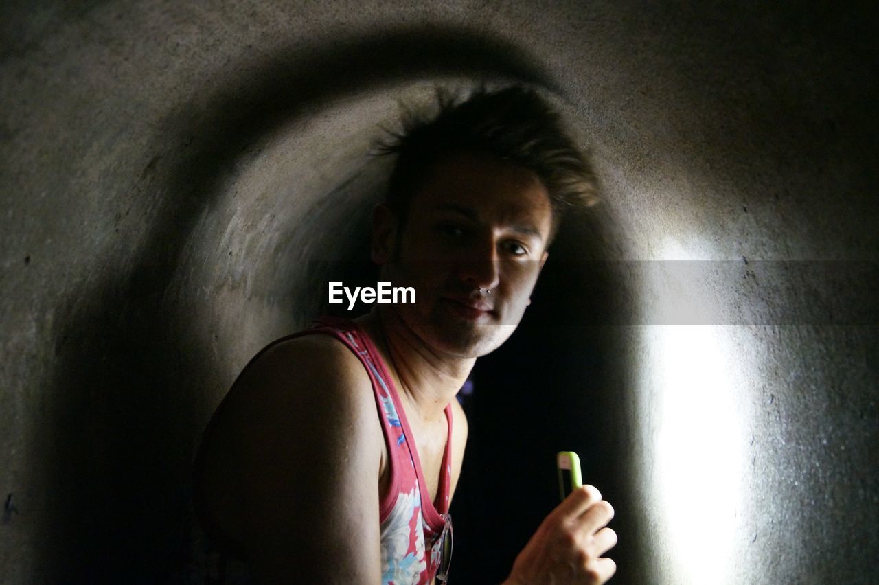 Portrait of young man holding mobile phone in tunnel