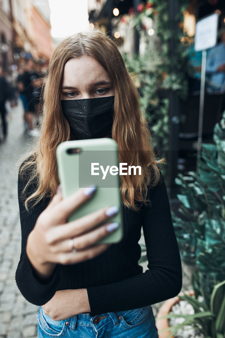 Girl wearing mask holding smart phone outdoors