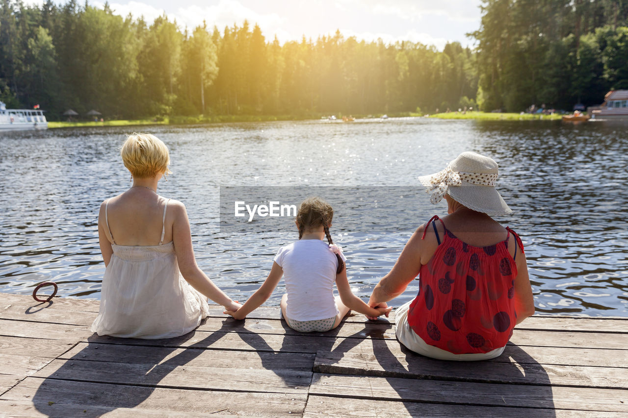 Rear view of girl sitting with mother and grandmother on pier over lake