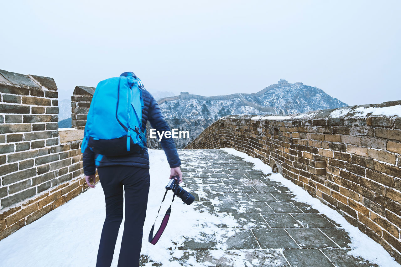 Full length rear view of man walking on snowcapped mountain