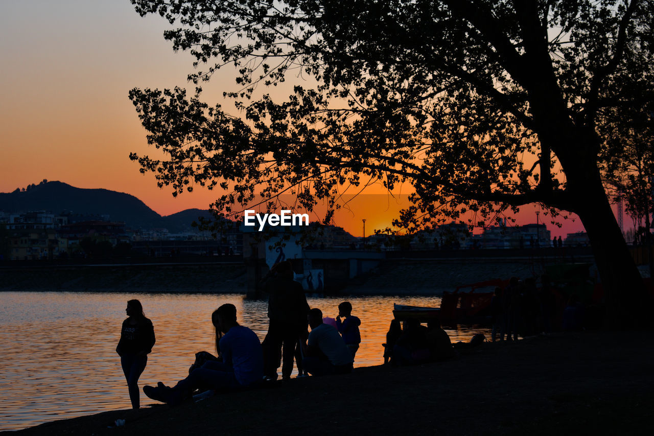 Silhouette of people sitting by lake during sunset