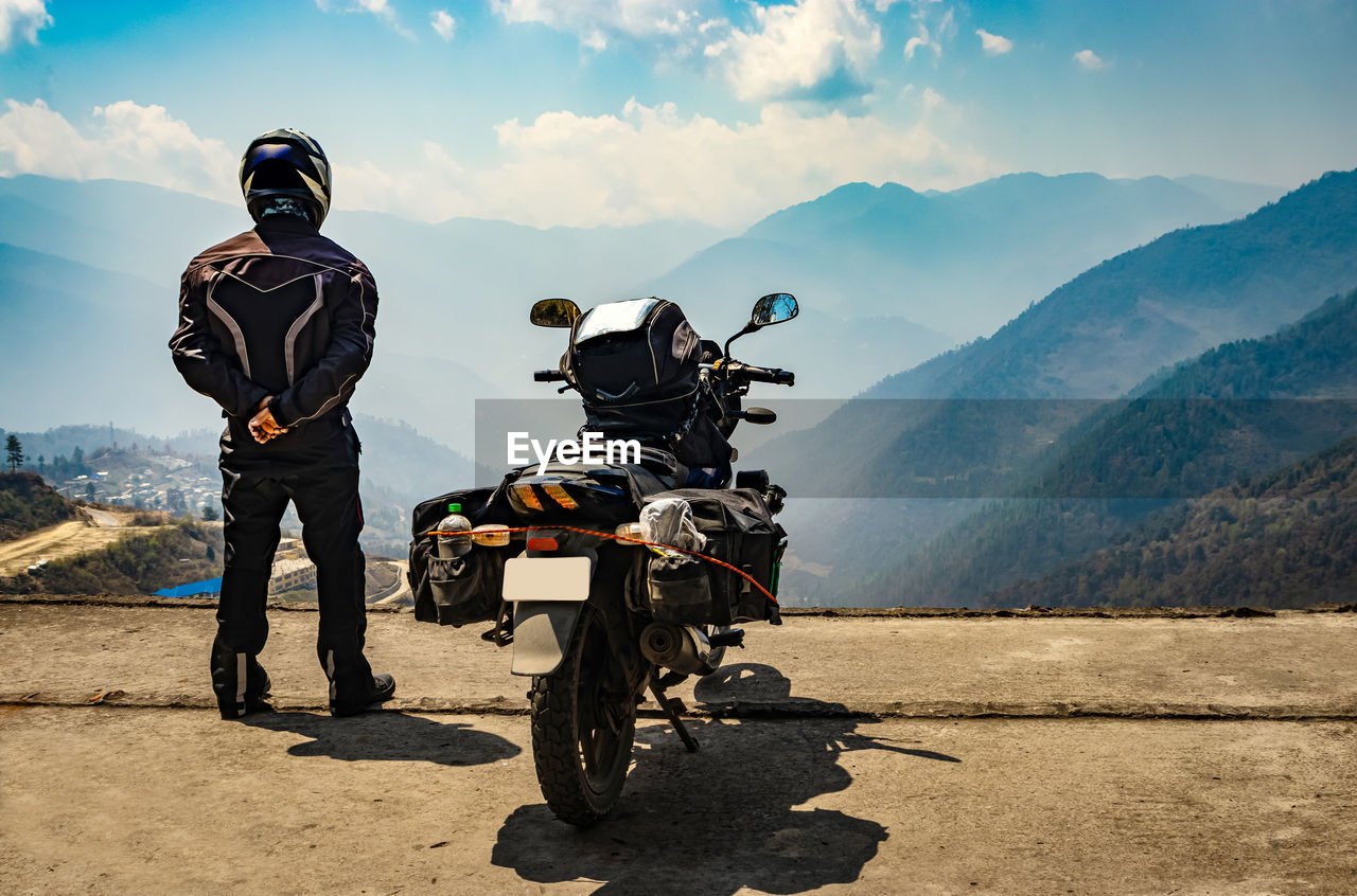 Man motorcyclist watching valley from hill top with his loaded motorcycle and pristine natural view